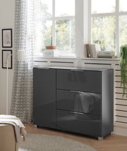 Moderne, dunkelgraue Kommode mit Hochglanzoberfläche, seitliche Perspektive, in einem hellen Raum mit großen Fenstern und dekorativen Elementen.