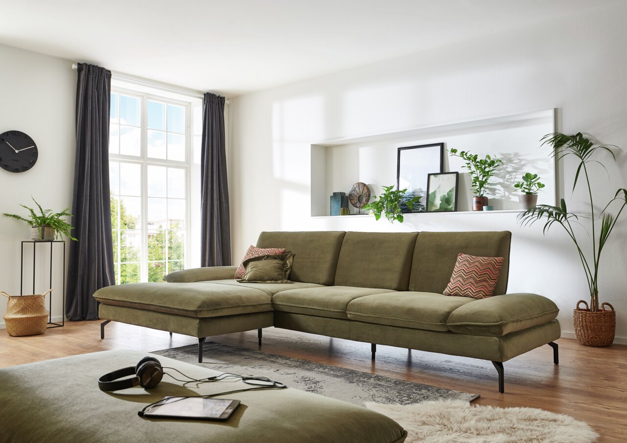 Grüne Longchairkombination in einem modernen Wohnzimmer, seitliche Perspektive, mit großen Fenstern und Pflanzen dekoriert.