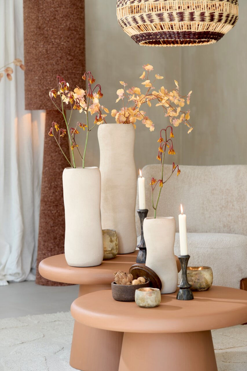 Light&Living Vase SERAFINA 38cm Drei elegante, cremefarbene Vasen mit Blumenarrangements auf einem runden, terrakottafarbenen Tisch, umgeben von Kerzen und dekorativen Elementen, aus einer seitlichen Perspektive betrachtet.
