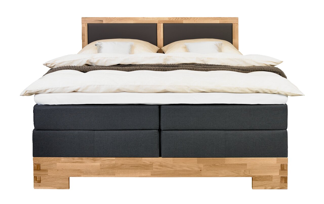 Frontale Ansicht eines stilvollen Boxspringbetts mit Holzrahmen und dunklem Stoffbezug, ausgestattet mit bequemer Bettwäsche und Kissen.