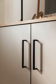 Nahaufnahme eines Schuhschranks mit zwei Türen, schwarzen Griffen und einer Sonnenbrille auf der Oberseite, seitliche Perspektive.