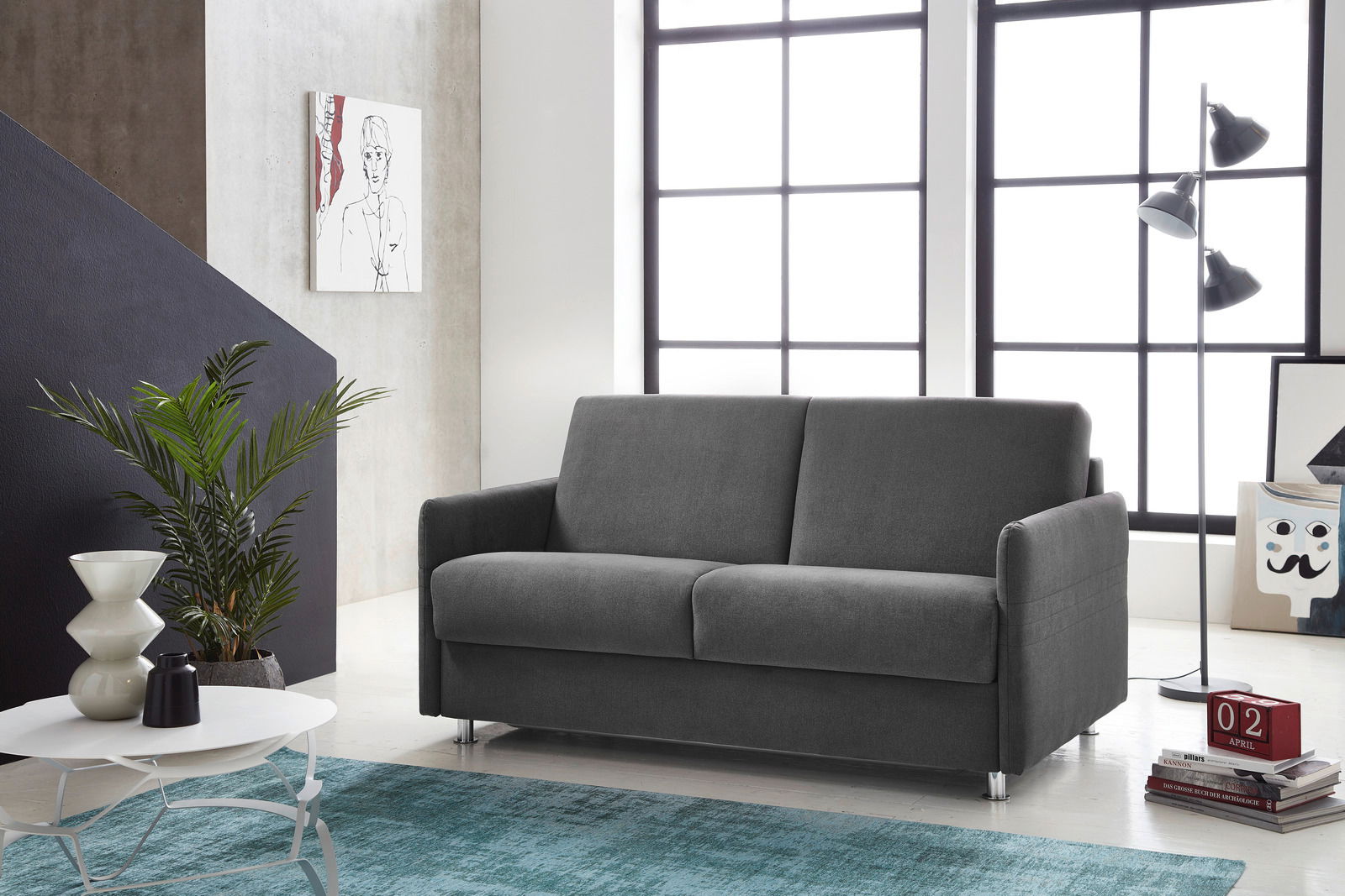 Graues Schlafsofa in modernem Wohnzimmer, seitliche Perspektive, mit großen Fenstern im Hintergrund.