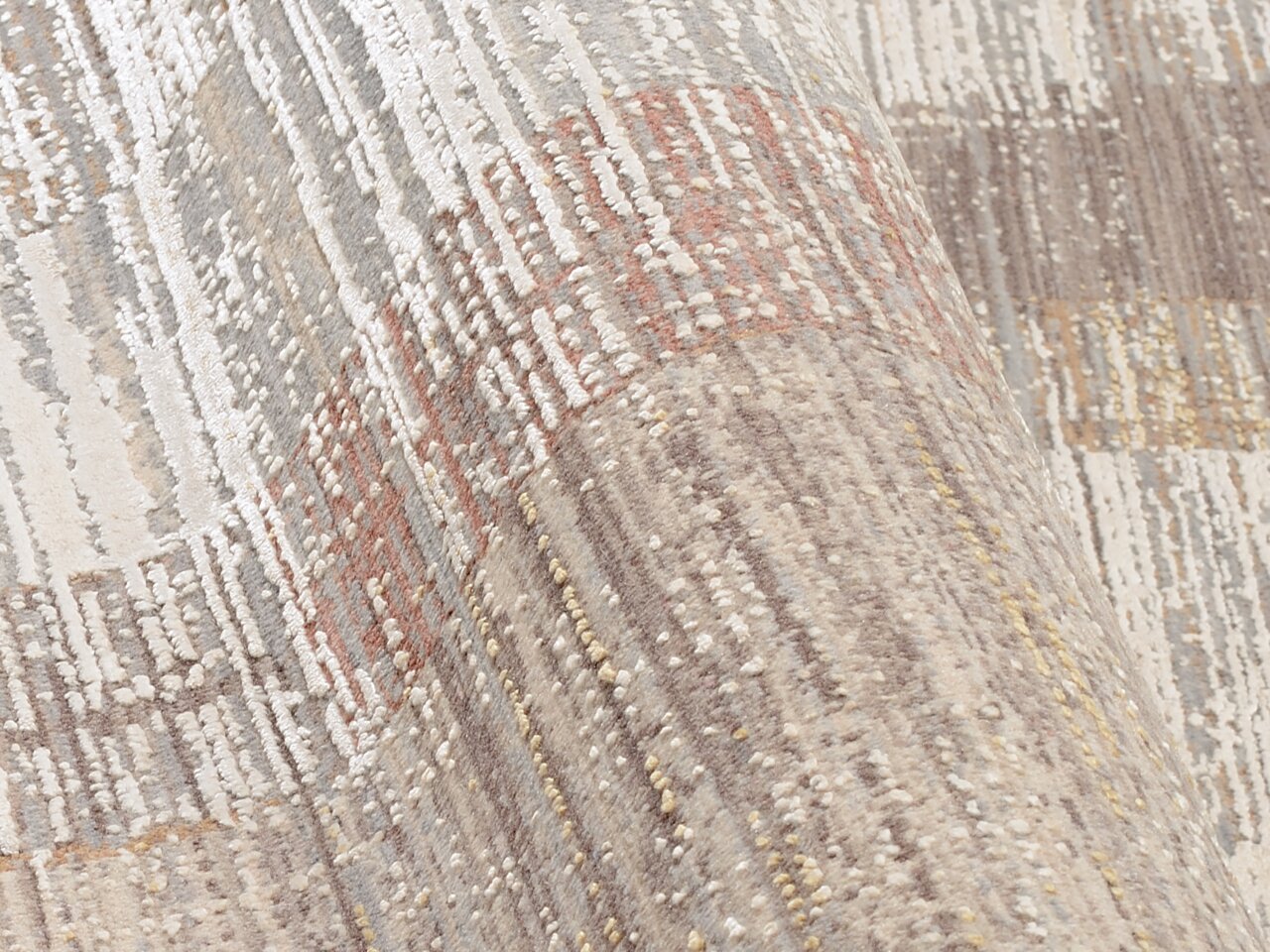 Nahaufnahme eines Designer-Teppichs mit abstraktem Muster in neutralen Tönen, perspektivisch von der Seite aufgenommen.