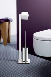 Freistehende WC-Garnitur aus poliertem Edelstahl mit Toilettenpapierhalter und Toilettenbürste neben einem weißen WC vor violetter Wand, Frontansicht in leicht schräger Perspektive von links.