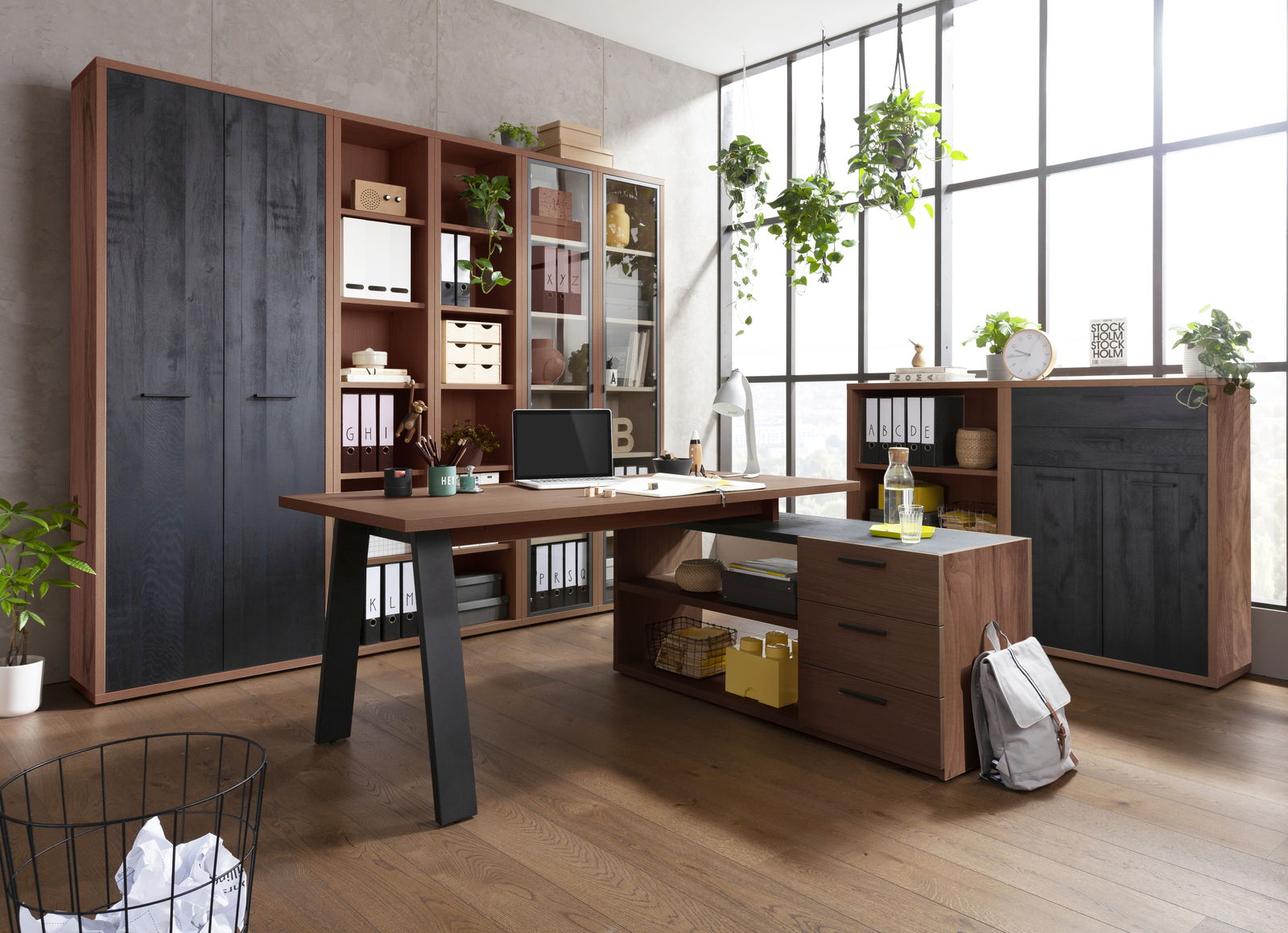 Moderne Büromöbel in einem hellen Raum mit großen Fenstern, bestehend aus einem Eckschreibtisch, Regalen und Schränken in Holzoptik. Perspektive von vorne.