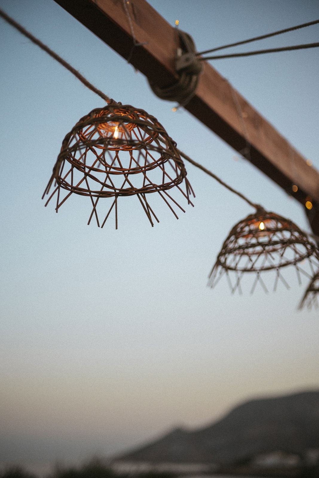 Outdoor-Lichterkette mit geflochtenen Lampenschirmen bei Sonnenuntergang, seitliche Perspektive