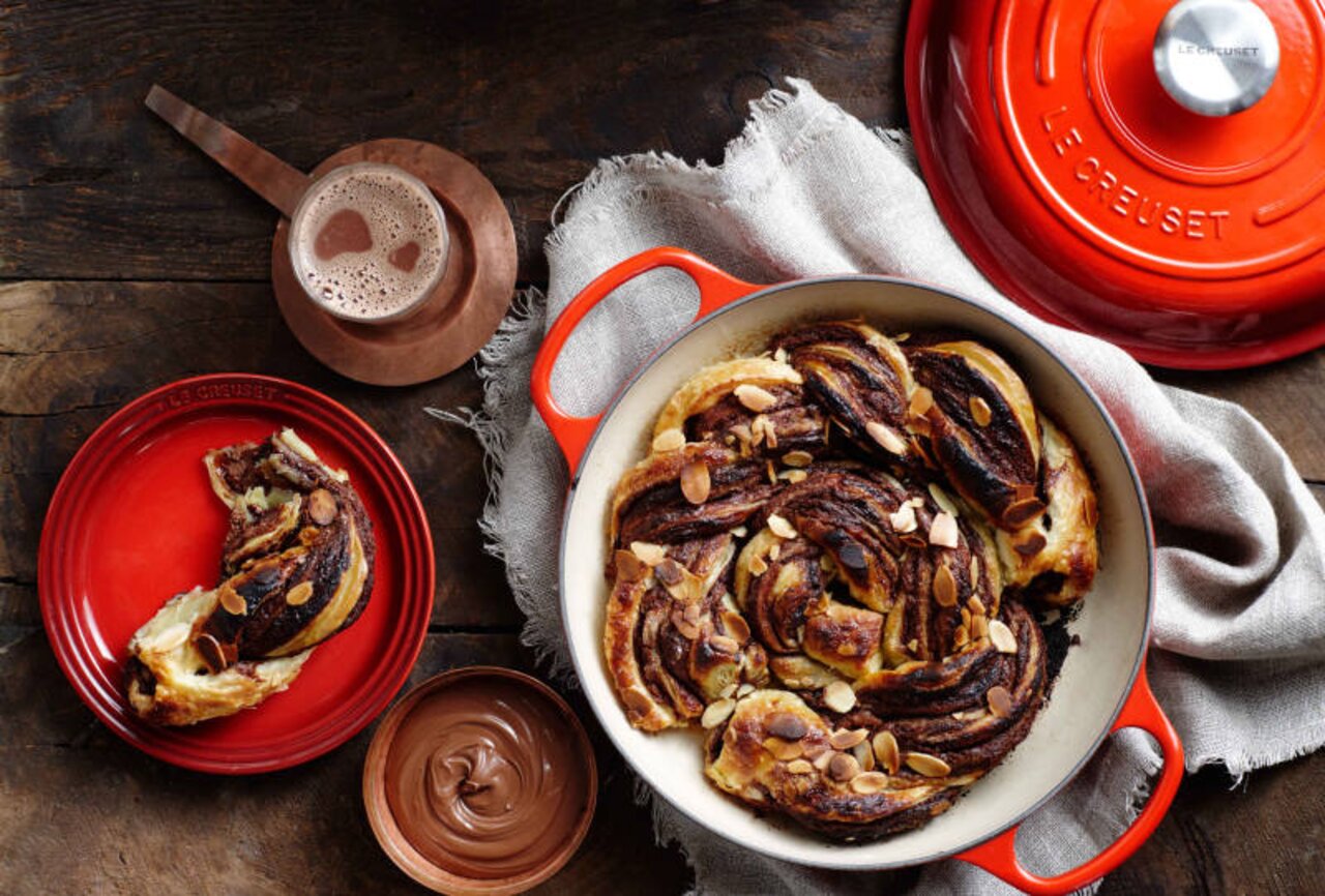 LE CREUSET Gourmet Profitopf 30cm Kirschrot SIGNATURE Gourmet Profitopf 30cm Kirsch von oben mit Gebäck und Mandeln, umgeben von Schokolade und Getränk.