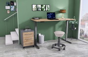 Modern elektrisch bureau in een stijlvol kantoor met een groene muur, een rolcontainer en een ergonomische kruk, gezien vanaf de zijkant.