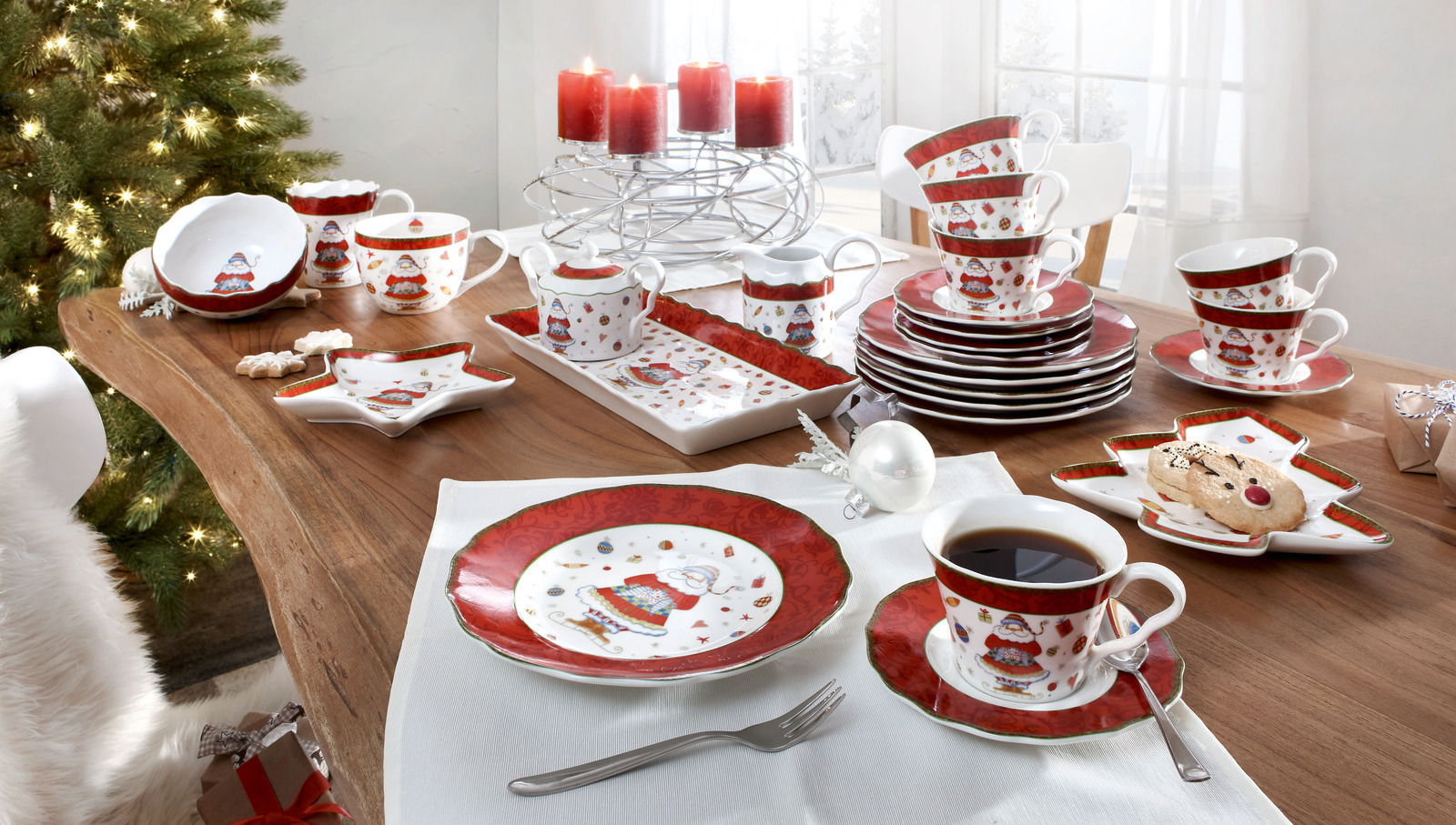 Weihnachtliches Kaffeeservice auf einem festlich gedeckten Tisch mit Kerzen und Weihnachtsbaum im Hintergrund, aus der Vogelperspektive fotografiert.