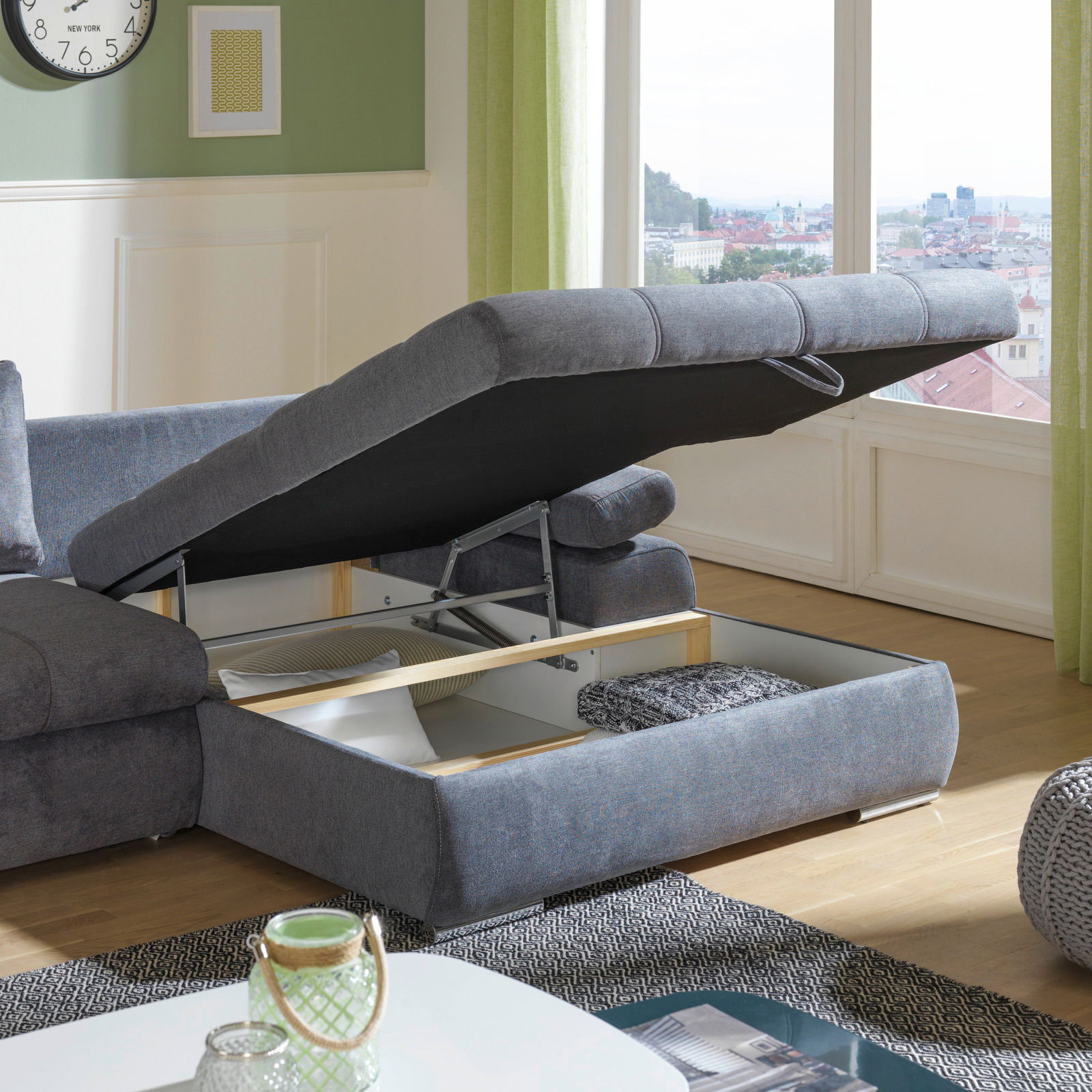 Graues Ecksofa mit Stauraum, geöffnete Ottomane, Tageslicht, Stadtblick im Hintergrund, Perspektive von der Seite