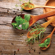 Holzlöffel mit frischen Kräutern wie Minze, Rosmarin und Basilikum auf rustikalem Holztisch, aus der Vogelperspektive fotografiert.