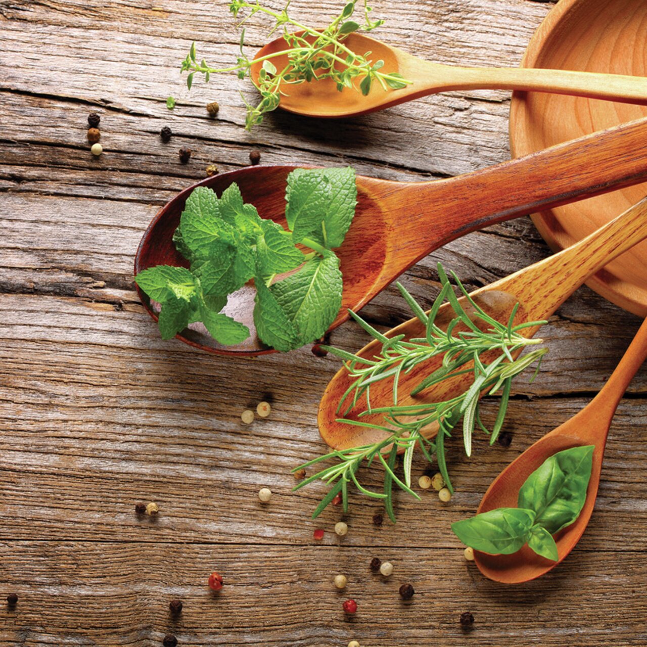 Holzlöffel mit frischen Kräutern wie Minze, Rosmarin und Basilikum auf rustikalem Holztisch, aus der Vogelperspektive fotografiert.
