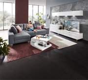 Moderner Couchtisch in Weiß mit zwei Ebenen, dekoriert mit Büchern und Gläsern, in einem stilvollen Wohnzimmer mit grauem Sofa und großen Fenstern, seitliche Perspektive.