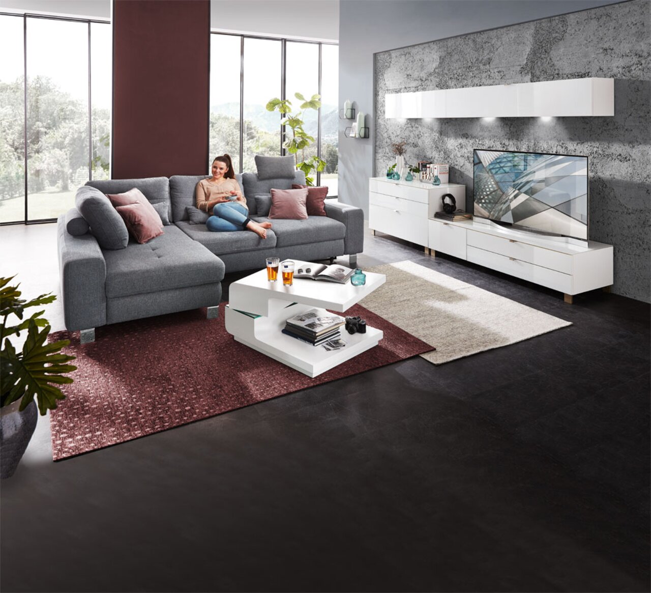 Moderner Couchtisch in Weiß mit zwei Ebenen, dekoriert mit Büchern und Gläsern, in einem stilvollen Wohnzimmer mit grauem Sofa und großen Fenstern, seitliche Perspektive.