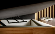 Nahaufnahme eines Boxspringbetts mit geöffnetem Stauraum, sichtbare Hebemechanik und Holzelementen, seitliche Perspektive.