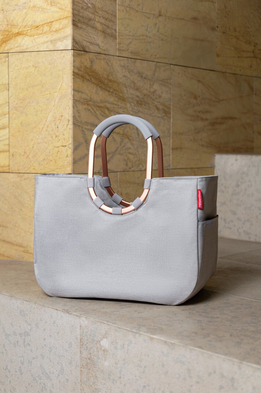 Graue Tasche mit ovalem Griff, auf einer Treppenstufe platziert, seitliche Perspektive.