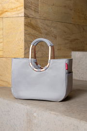 Graue Tasche mit ovalem Griff, auf einer Treppenstufe platziert, seitliche Perspektive.