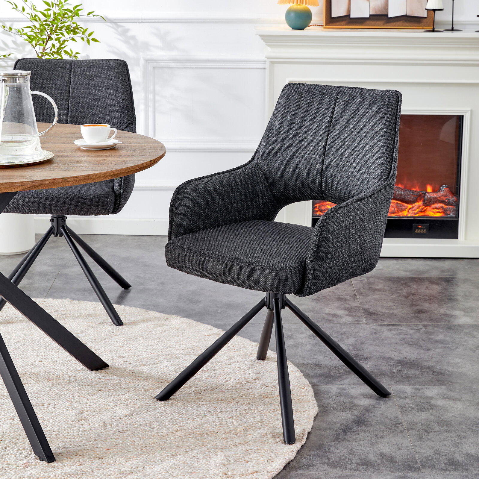 Dunkelgrauer, gepolsterter Esszimmer-Drehstuhl mit Armlehnen und schwarzem Metall-Sternfuß neben rundem Holztisch, in schräger Vorderansicht im Wohn-/Essbereich.