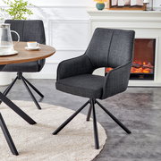 Dunkelgrauer, gepolsterter Esszimmer-Drehstuhl mit Armlehnen und schwarzem Metall-Sternfuß neben rundem Holztisch, in schräger Vorderansicht im Wohn-/Essbereich.