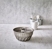 Gugelhupfform aus Metall, seitliche Perspektive, auf einer Küchenarbeitsplatte mit Küchenutensilien im Hintergrund.