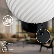 Nahaufnahme in seitlicher Perspektive: weiße, geriffelte LED-Tischlampe mit schwarzem Sockel, USB-C-Ladeanschluss und Ein-/Aus-Schalter, Detailansicht der Unterseite mit Standfüßen