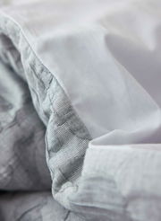 Nahaufnahme von Bettwäsche in Weiß und Grau mit feinen Streifen und Mustern, aus der Seitenperspektive aufgenommen.