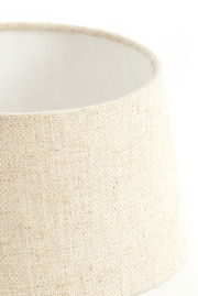 Nahaufnahme eines runden, cremefarbenen Lampenschirms aus grobem Stoff, seitliche Perspektive.