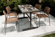Vier Stapelsessel aus Rattan mit Metallrahmen um einen modernen Gartentisch, Perspektive von schräg oben.