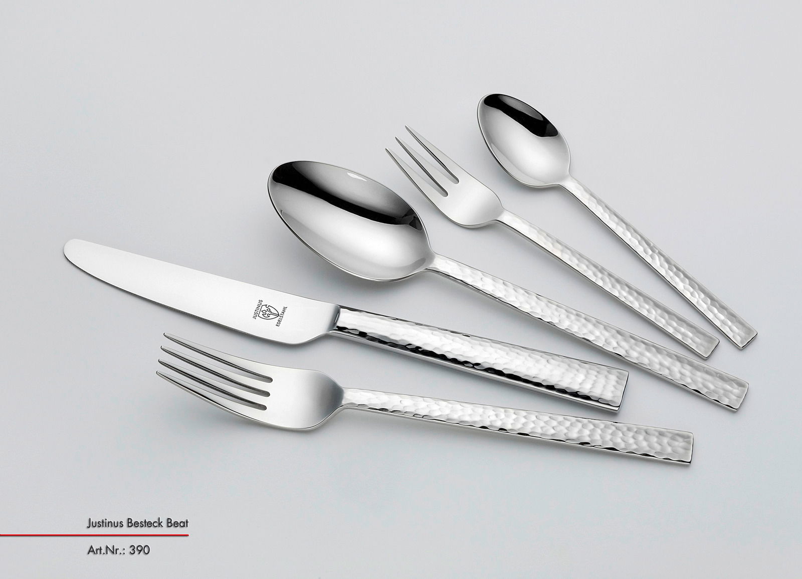 Set aus glänzendem Besteck mit gehämmerten Griffen, bestehend aus Messer, Gabel, Löffel und Teelöffel, in schräger Draufsicht.