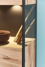 Detailansicht eines Highboards mit Holzoptik und Glaselementen, beleuchtet von oben.