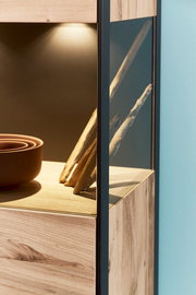 Detailansicht eines Highboards mit Holzoptik und Glaselementen, beleuchtet von oben.