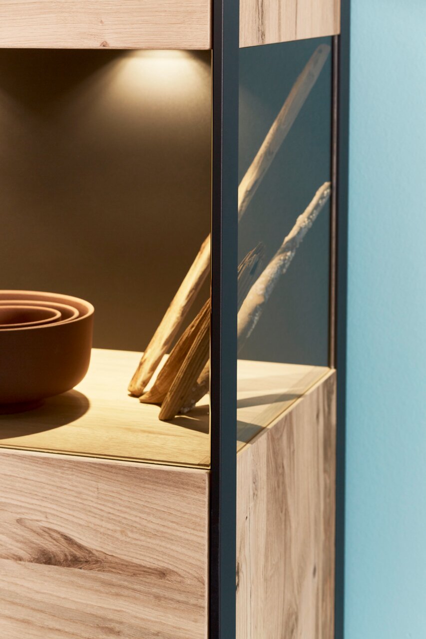 Detailfoto van een hoogkast met houtlook en glazen elementen, van bovenaf verlicht.