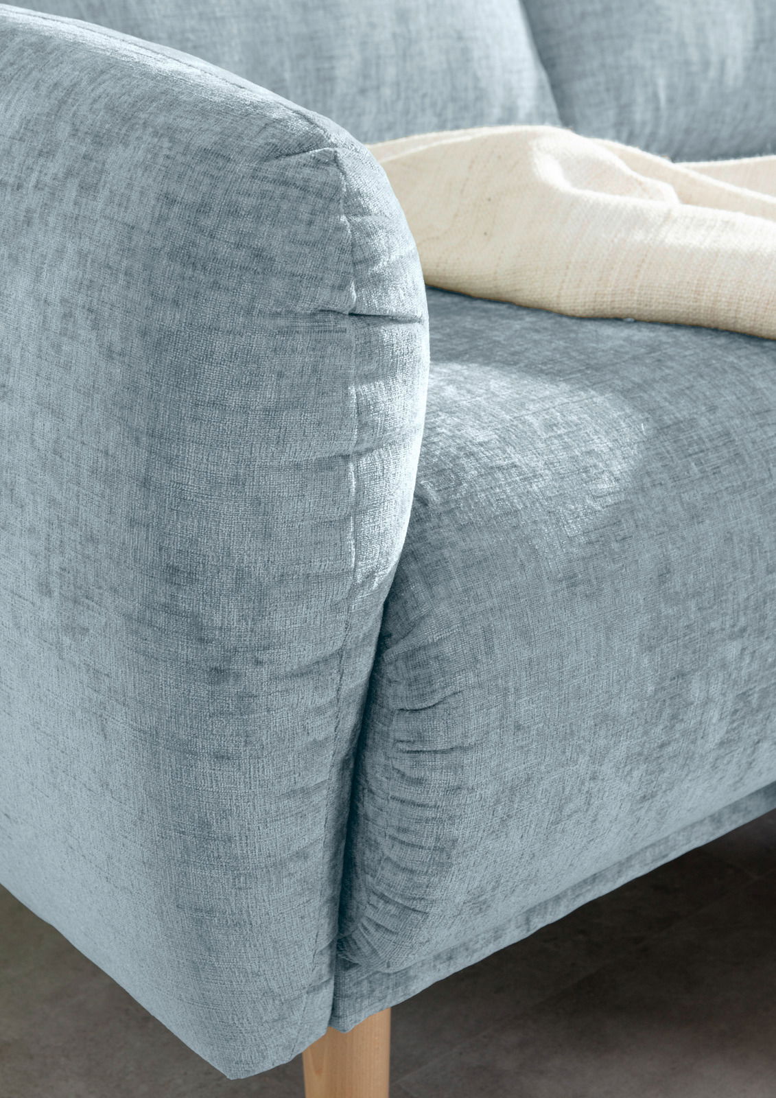 Nahaufnahme einer hellblauen Sofaecke mit Holzbeinen, von der Seite betrachtet.