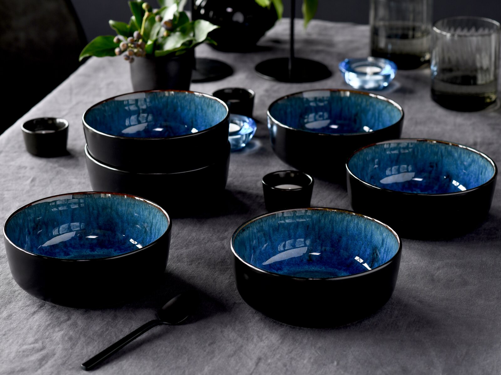 Schwarze Keramikschalen mit blau glasierter Innenseite auf grauer Tischdecke, dekorativ arrangiert, Perspektive: leicht von oben in schräger Frontansicht.
