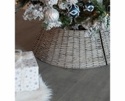 Nahaufnahme eines geflochtenen Baumrings aus Weide, der den unteren Teil eines Weihnachtsbaums umgibt, mit dekorativen Kugeln und einem Geschenk im Vordergrund.