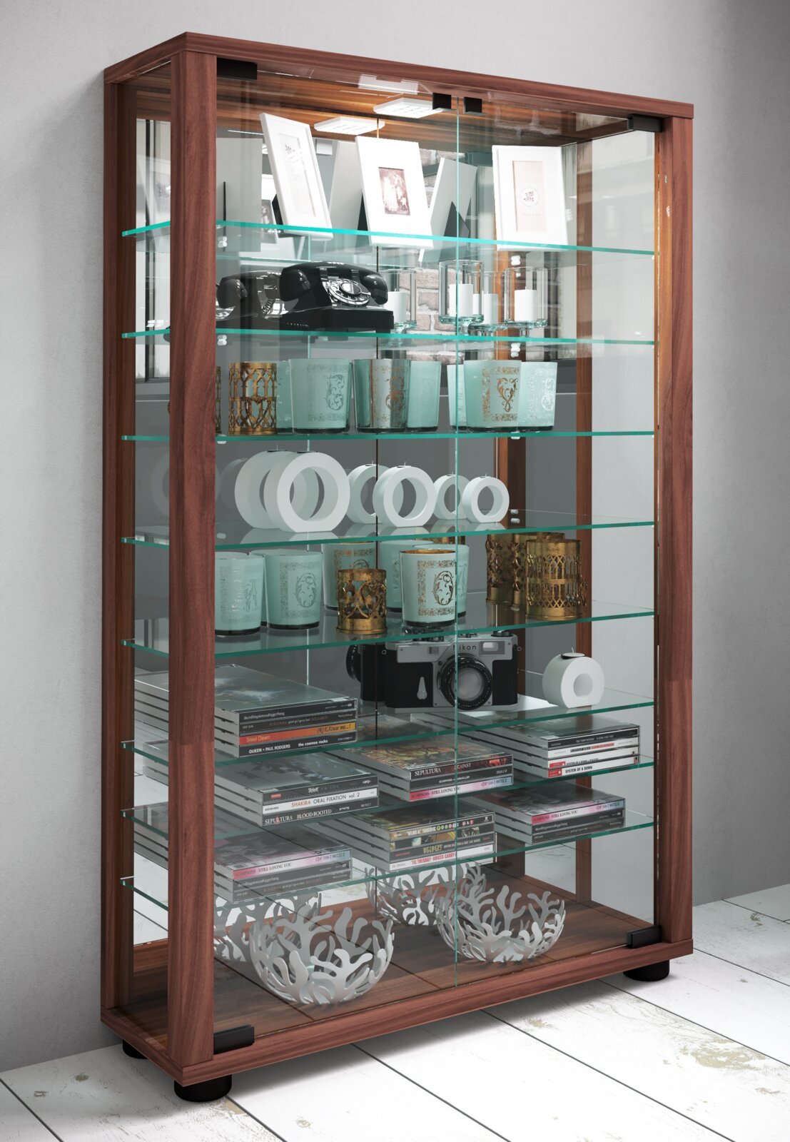 Holz-Glas-Vitrine mit mehreren Glasböden und Glastüren, bestückt mit Dekoartikeln, Telefon, Kamera und CDs, in schräger Frontansicht von links