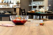 Glas-Schüssel mit optischem Design, gefüllt mit roten Früchten, auf einem Tisch in einem Esszimmer, seitliche Perspektive