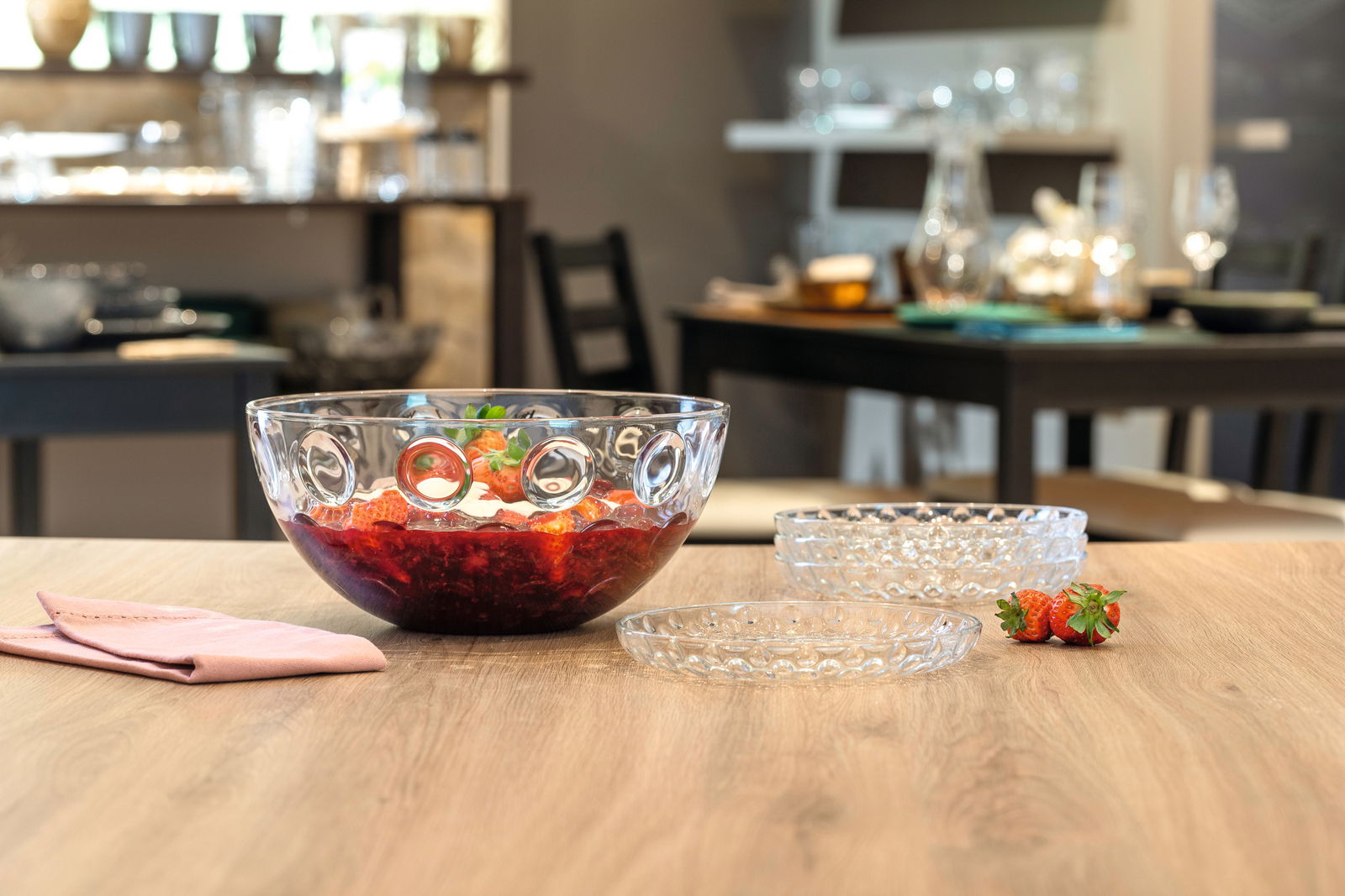 Glas-Schüssel mit optischem Design, gefüllt mit roten Früchten, auf einem Tisch in einem Esszimmer, seitliche Perspektive