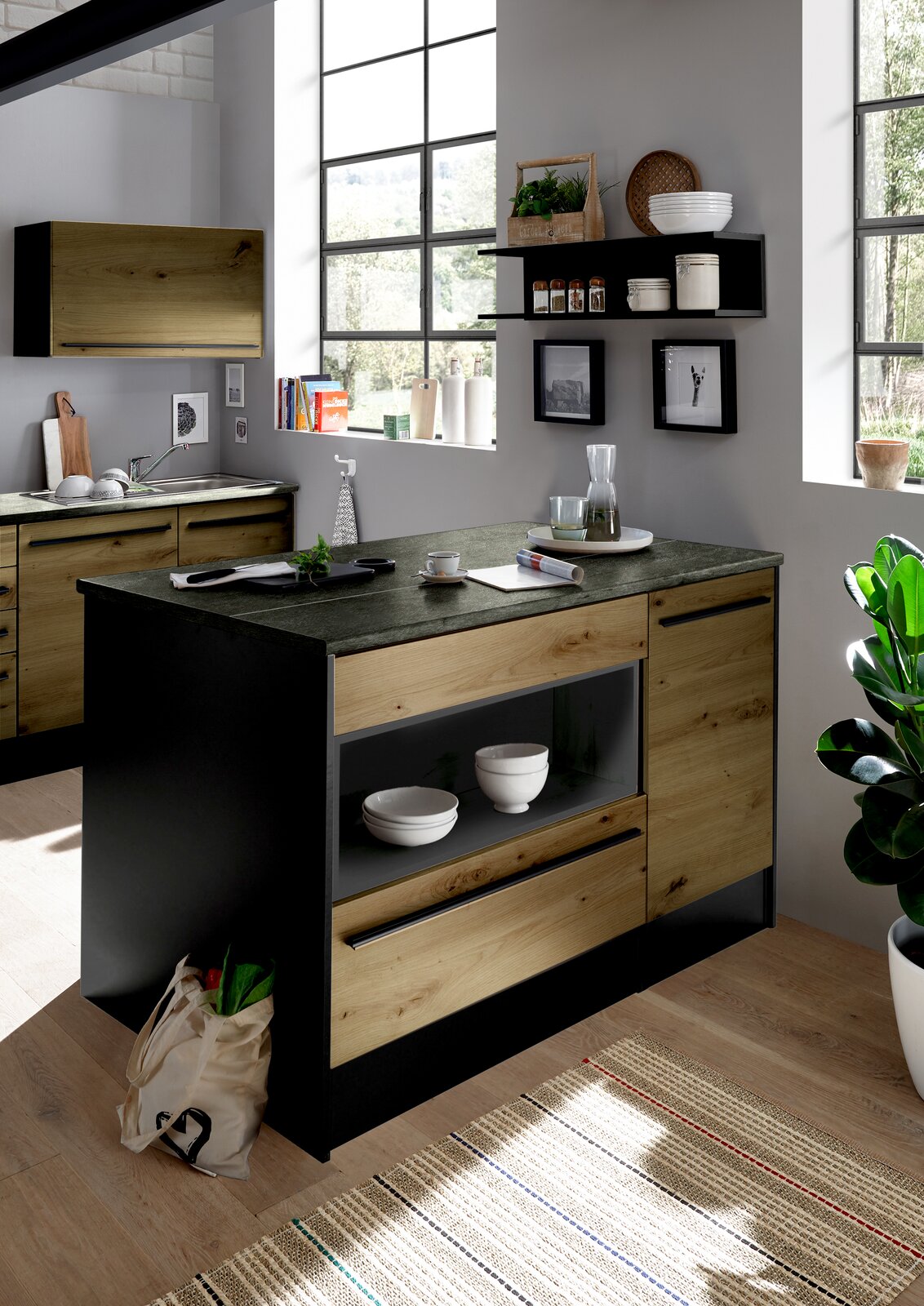 Moderne Kücheninsel aus Holz und dunklem Material, mit Regalen und Schubladen, in einer hellen Küche mit großen Fenstern, seitliche Perspektive.