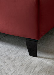 Nahaufnahme eines Boxspringbettbeins mit rotem Stoffbezug und schwarzem Holzfuß auf hellem Teppichboden.