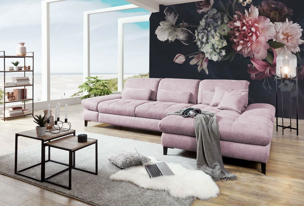 Rosa Ecksofa in modernem Wohnzimmer mit Blick auf das Meer, dekoriert mit Blumenwand und stilvollen Möbeln, seitliche Perspektive.