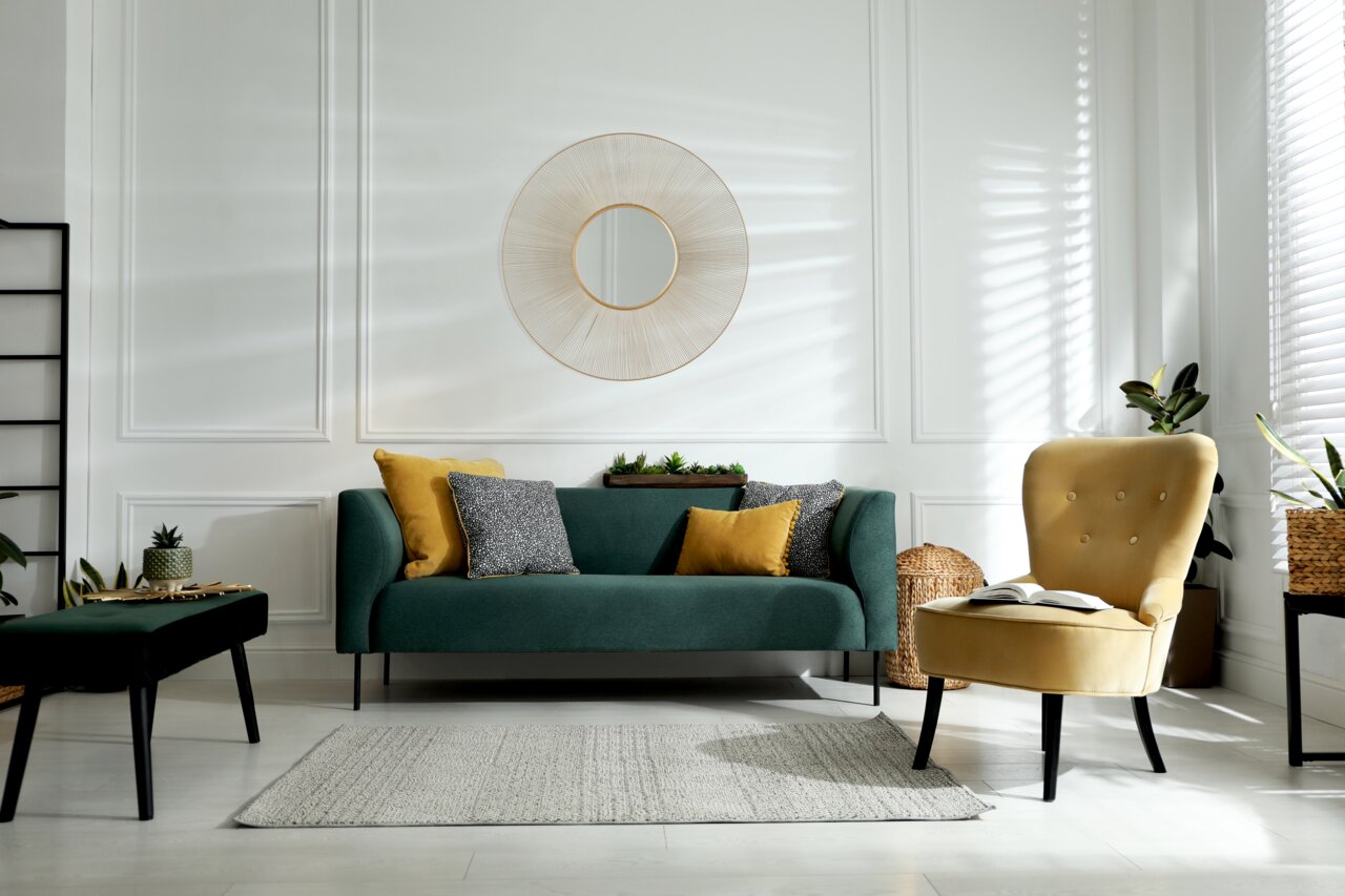 Runder Wandspiegel mit dekorativem Rahmen über einem grünen Sofa in einem stilvoll eingerichteten Wohnzimmer, seitliche Perspektive.