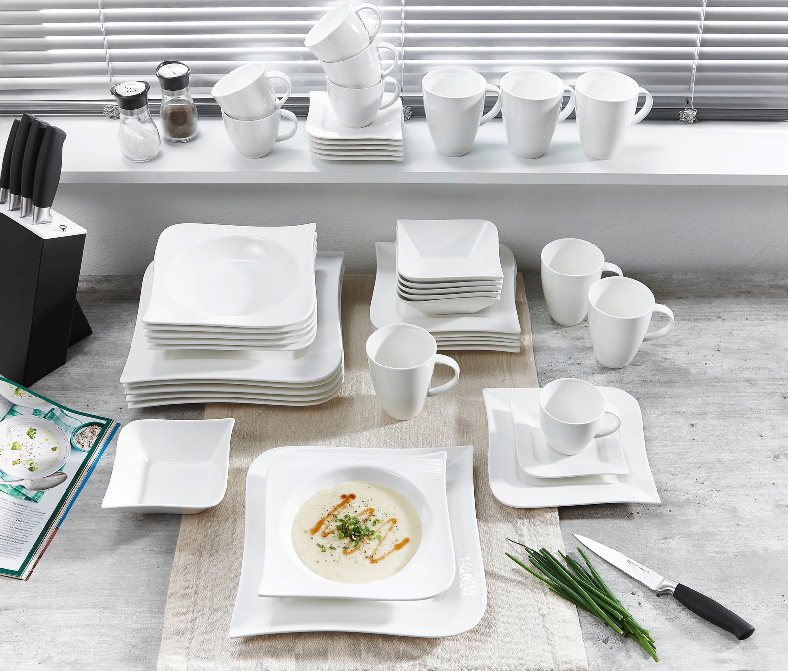 Vogelperspektive auf ein 42-teiliges Kombiservice-Set 'Melodie' mit weißen Tellern, Tassen und Schalen auf einem Tisch arrangiert.