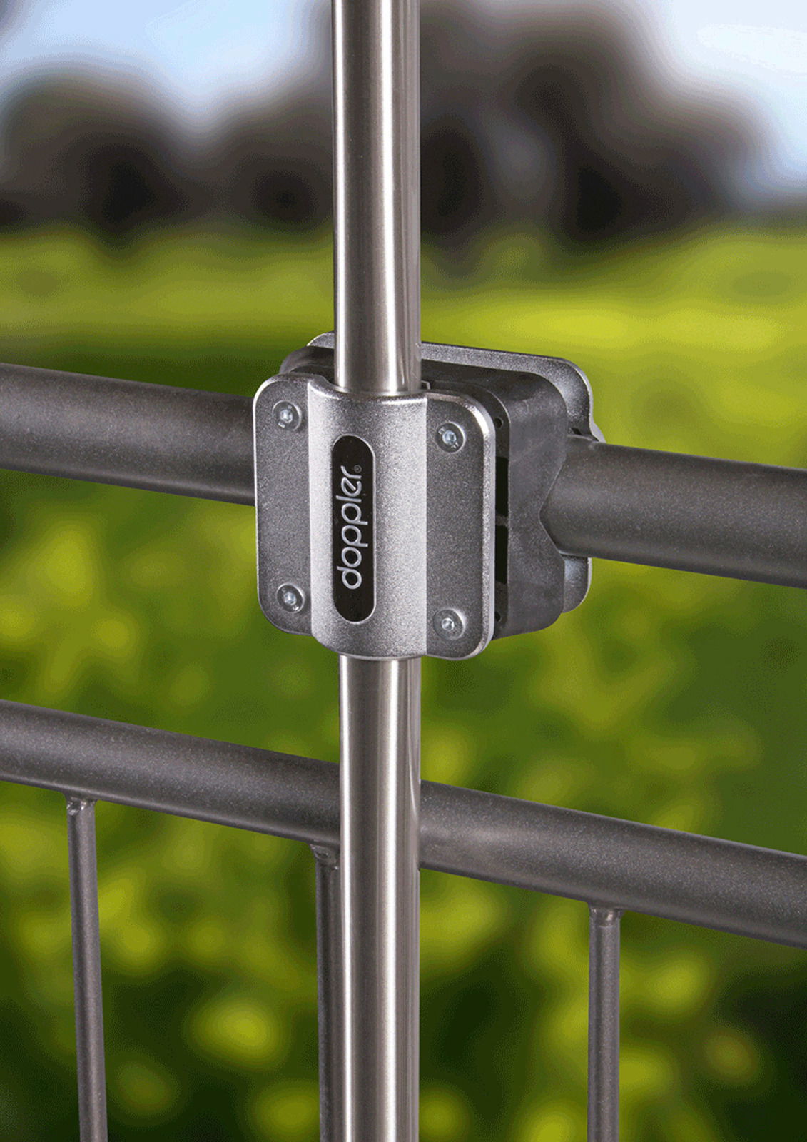 Nahaufnahme einer Balkonklammer aus Metall, die an einem Geländer befestigt ist, mit einem grünen, unscharfen Hintergrund.