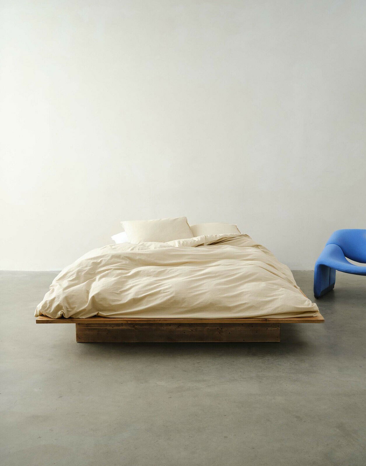 Bett mit beiger Bettwäsche in einem minimalistischen Raum, frontal fotografiert