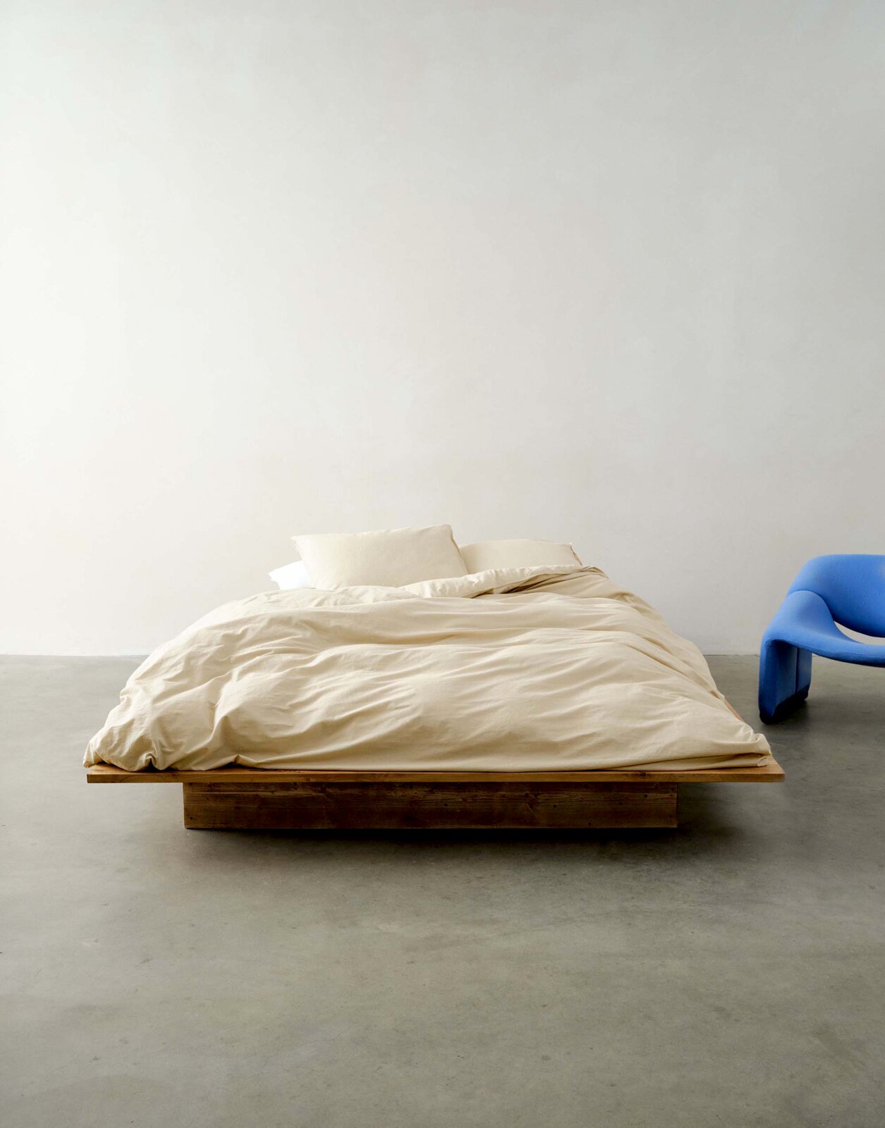 Bett mit beiger Bettwäsche in einem minimalistischen Raum, frontal fotografiert