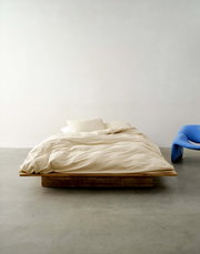 Bed met beige beddengoed in een minimalistische ruimte, van voren gefotografeerd