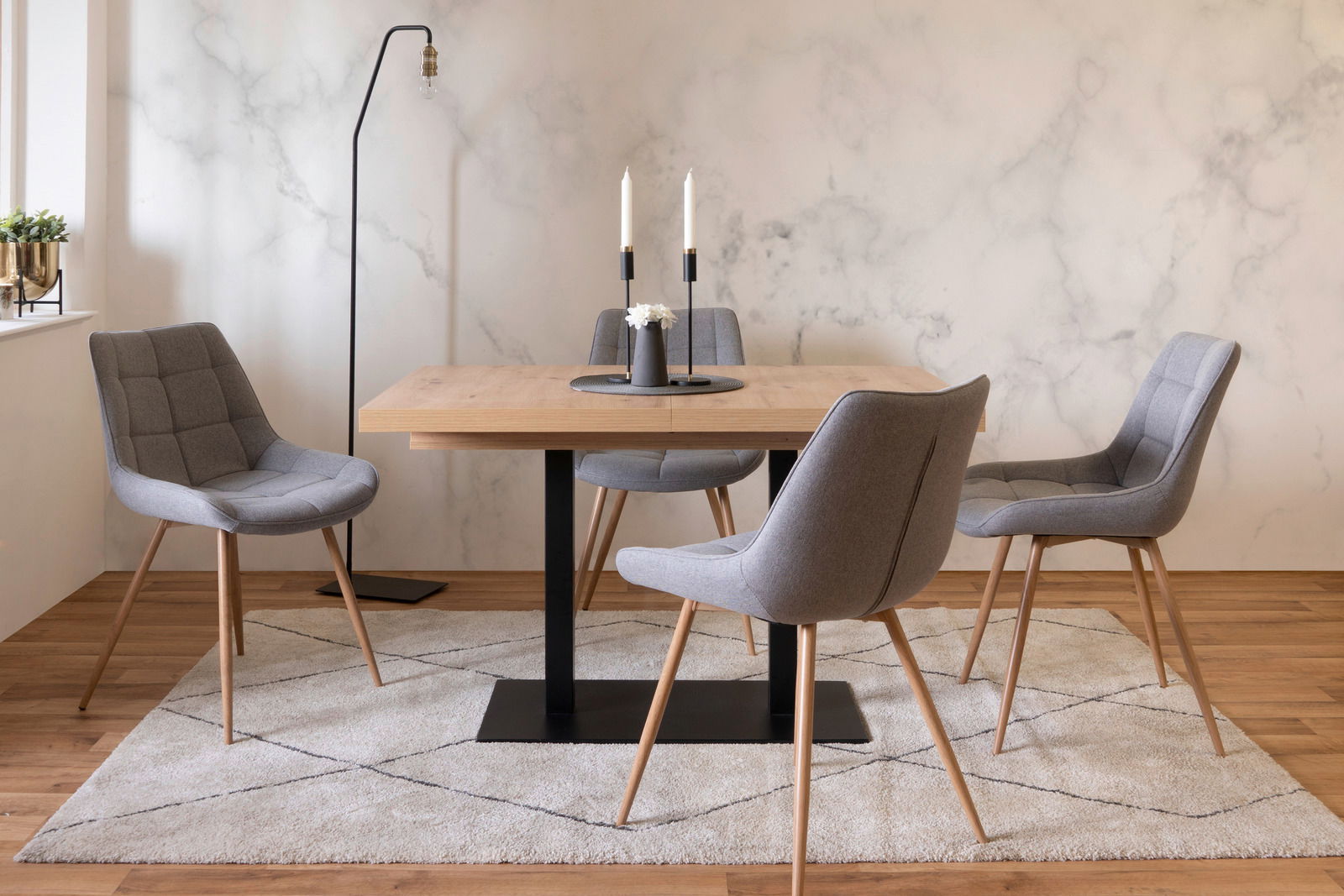 Moderner Esstisch mit Holzplatte und schwarzem Metallgestell, umgeben von vier grauen Polsterstühlen auf einem Teppich, seitliche Perspektive.