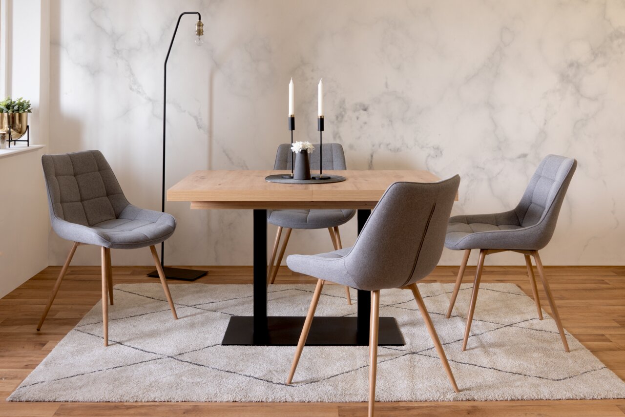 Moderner Esstisch mit Holzplatte und schwarzem Metallgestell, umgeben von vier grauen Polsterstühlen auf einem Teppich, seitliche Perspektive.
