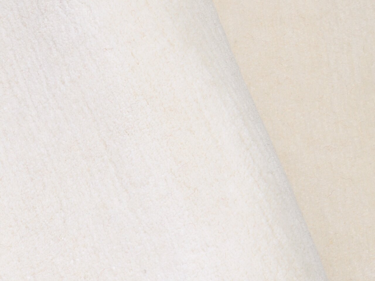 Nahaufnahme eines cremefarbenen Wollteppichs mit weicher Textur.